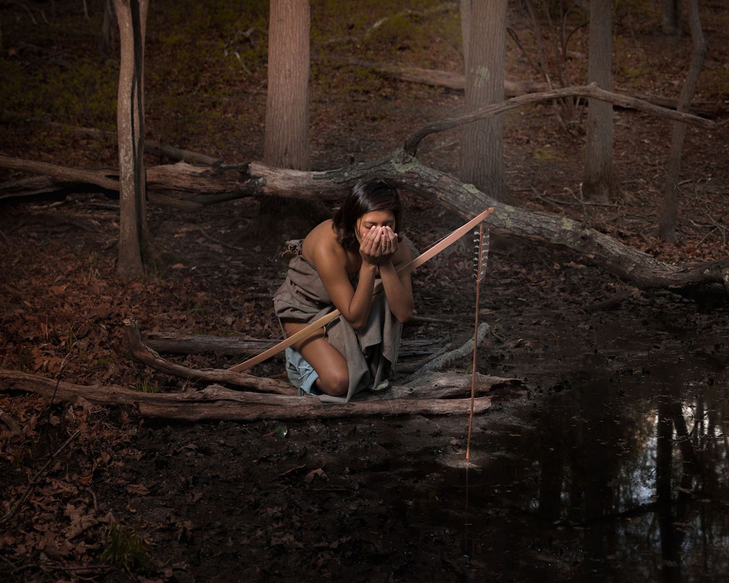 "Manitou Hill" by Jeremey Dennis. Photograph of a Native American in traditional clothing drinking from a stream.