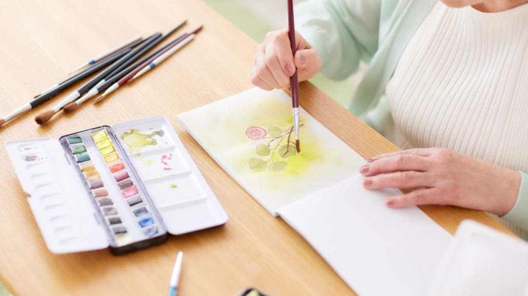 older woman paints a watercolor of a flower